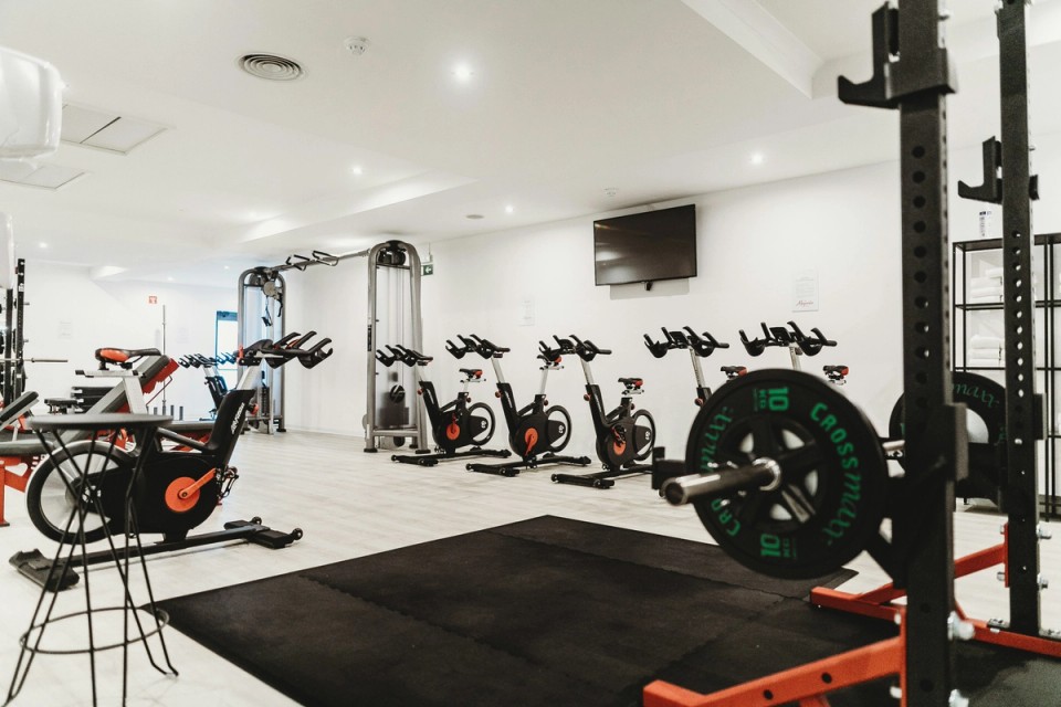 Modern fitness gym filled with squat racks, stationary bikes, weightlifting equipment, and resistance machines, representing the equipment-focused approach commonly used in contemporary athletic training.
