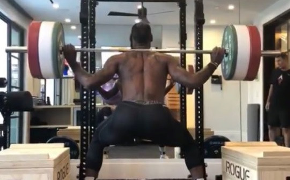 Professional athlete performing a heavy barbell back squat with multiple weight plates in a gym, illustrating traditional strength training methods commonly used to improve athletic performance.