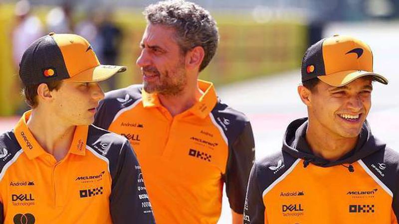 Oscar Piastri, team principal Andrea Stella and Lando Norris talking, all in orange McLaren team clothing.