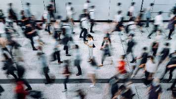 A crowd of commuters blurred in motion around one person standing still.