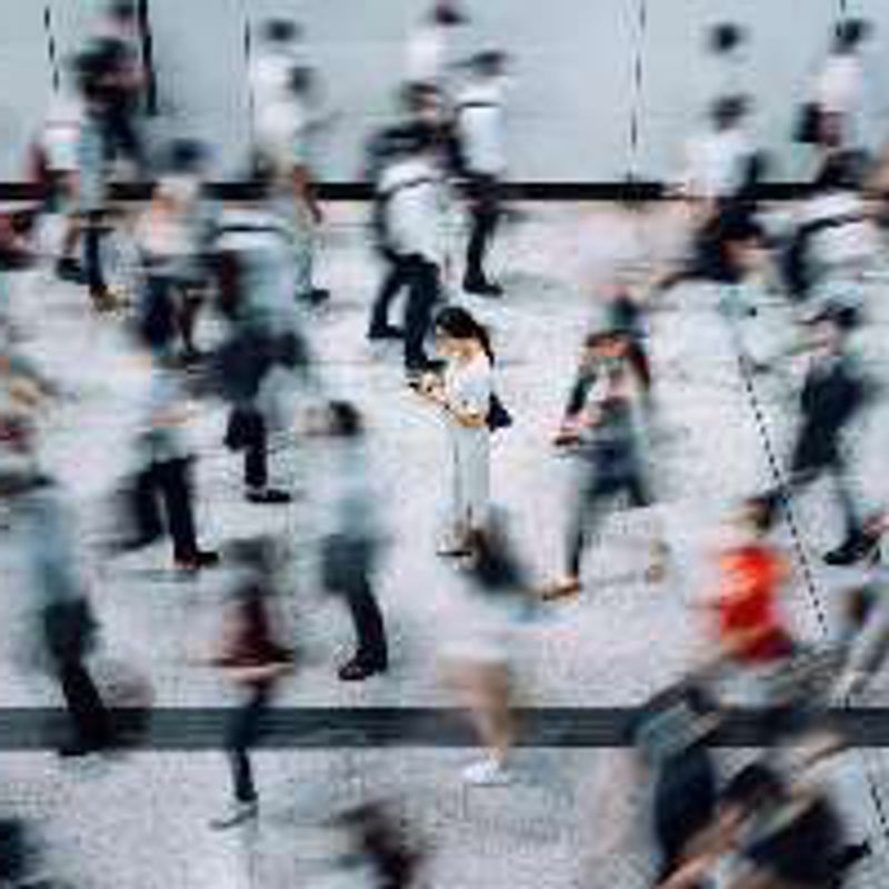 A crowd of commuters blurred in motion around one person standing still.