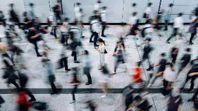 A crowd of commuters blurred in motion around one person standing still.