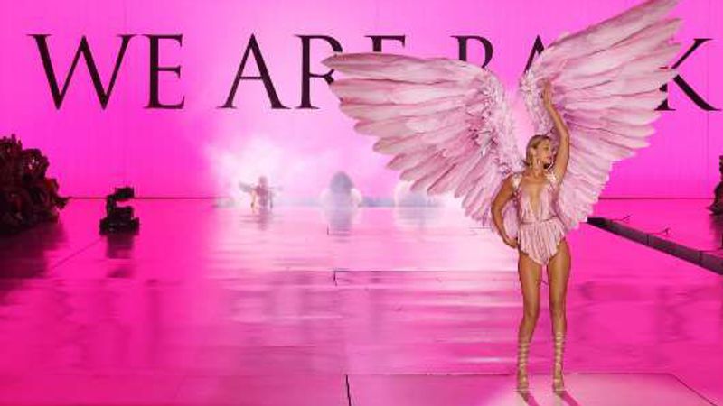 Gigi Hadid on a bright pink runway wearing large pink feathered wings, under the words “We are back”.