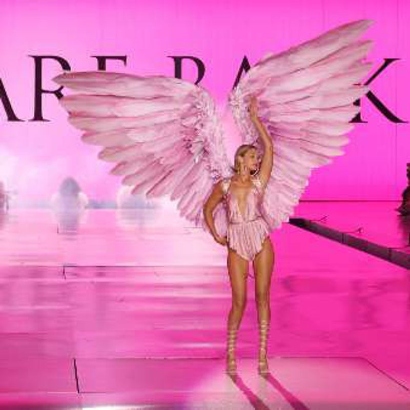Gigi Hadid on a bright pink runway wearing large pink feathered wings, under the words “We are back”.