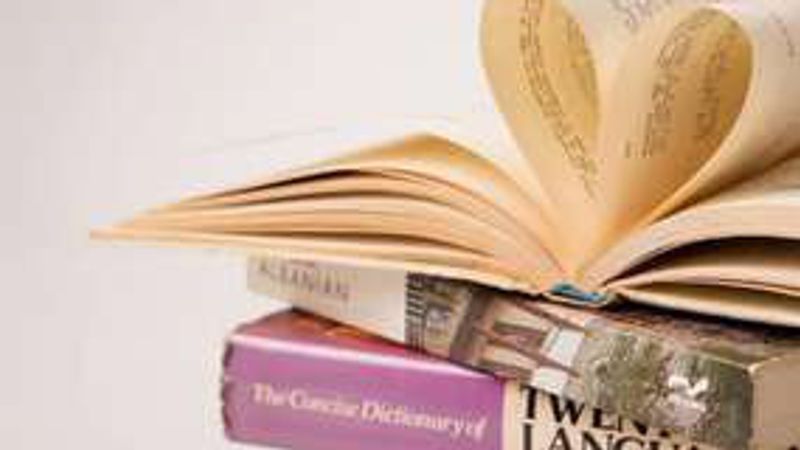An open book with pages curled into a heart, lying on a stack of language dictionaries.
