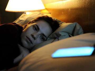 A woman lies awake in bed beside a glowing phone, in a still from Black Mirror.