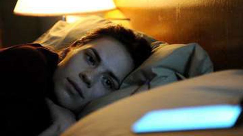 A woman lies awake in bed beside a glowing phone, in a still from Black Mirror.