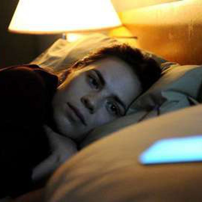 A woman lies awake in bed beside a glowing phone, in a still from Black Mirror.
