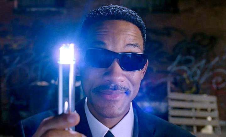 Will Smith in black sunglasses holds up a glowing neuralyzer.