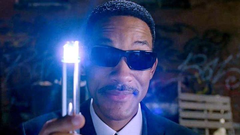 Will Smith in black sunglasses holds up a glowing neuralyzer.