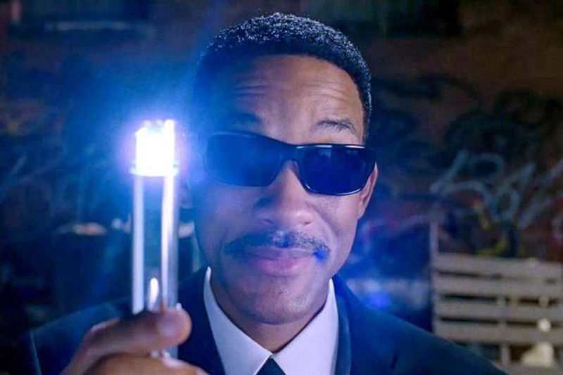Will Smith in black sunglasses holds up a glowing neuralyzer.