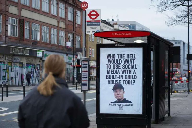 A woman walks past a London bus stop poster of Elon Musk reading “Who the hell would want to use social media with a built-in child abuse tool?”