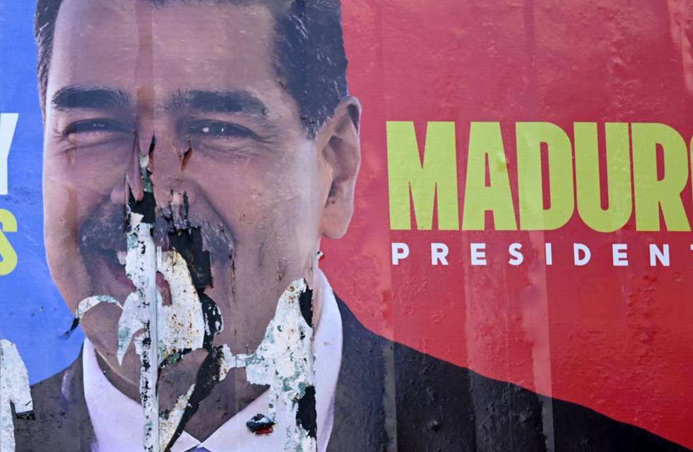 A torn and burned election billboard showing Nicolás Maduro's face beside the words “Maduro Presidente”.