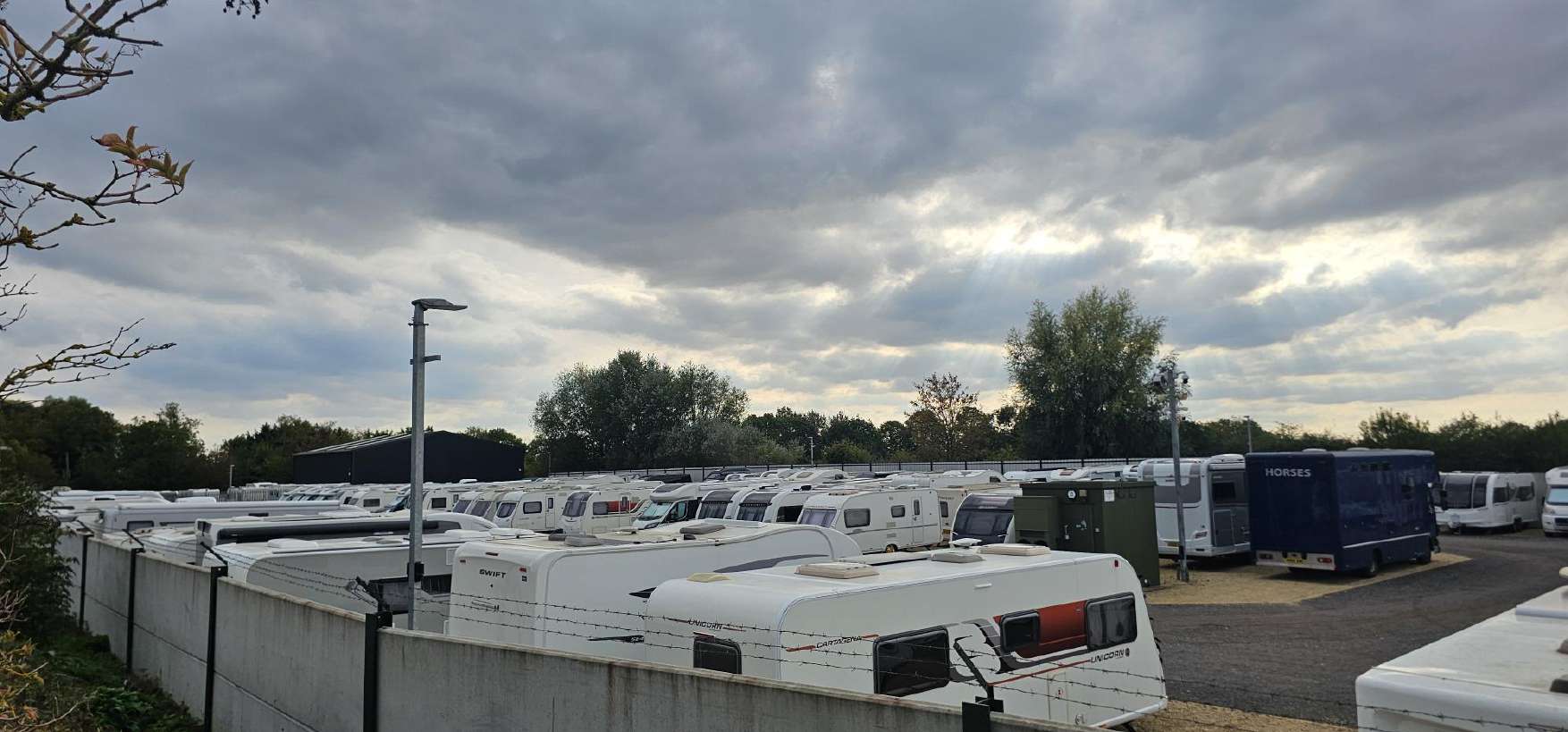 The 2.4m concrete perimeter wall topped with barbed wire, with caravans behind it