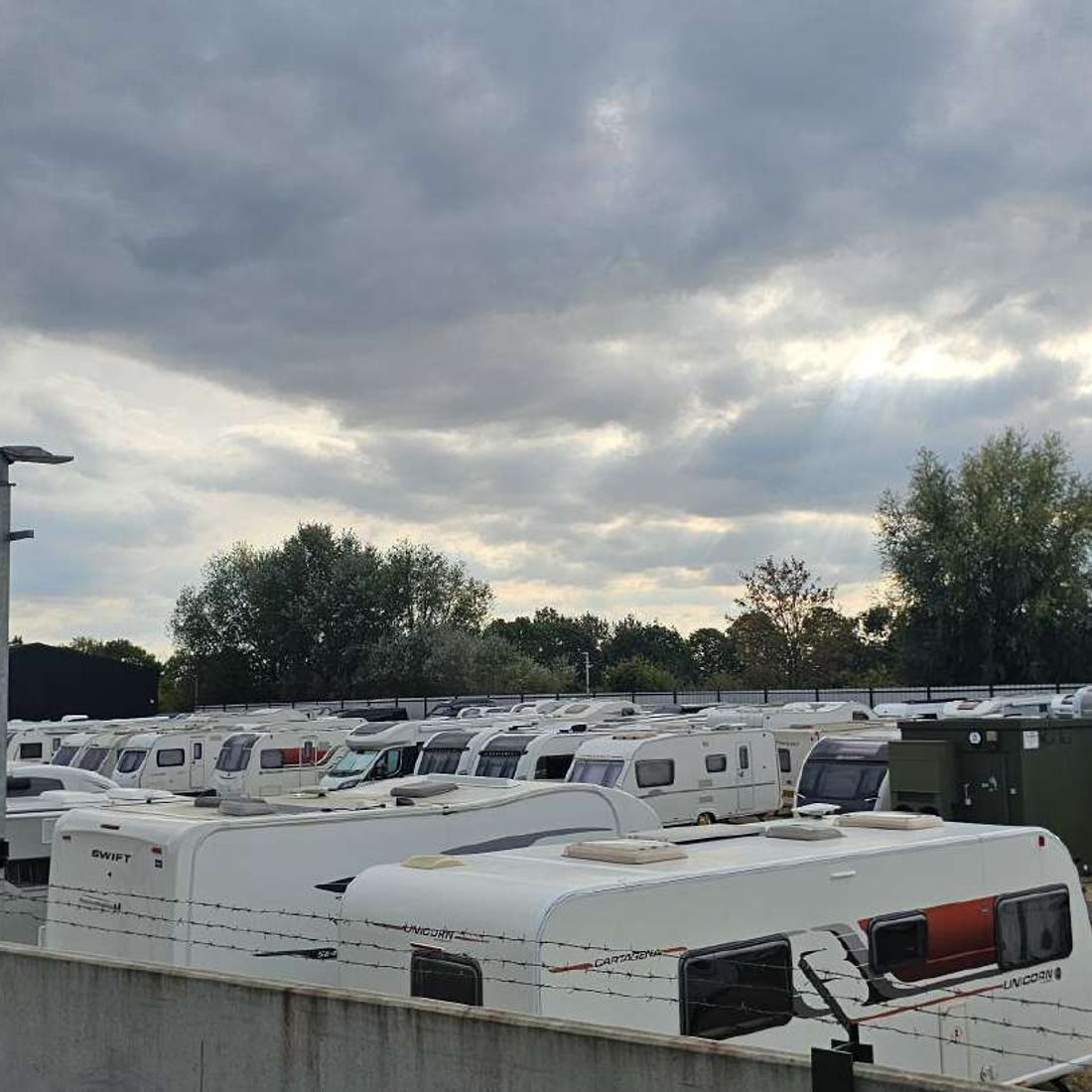 The 2.4m concrete perimeter wall topped with barbed wire, with caravans behind it