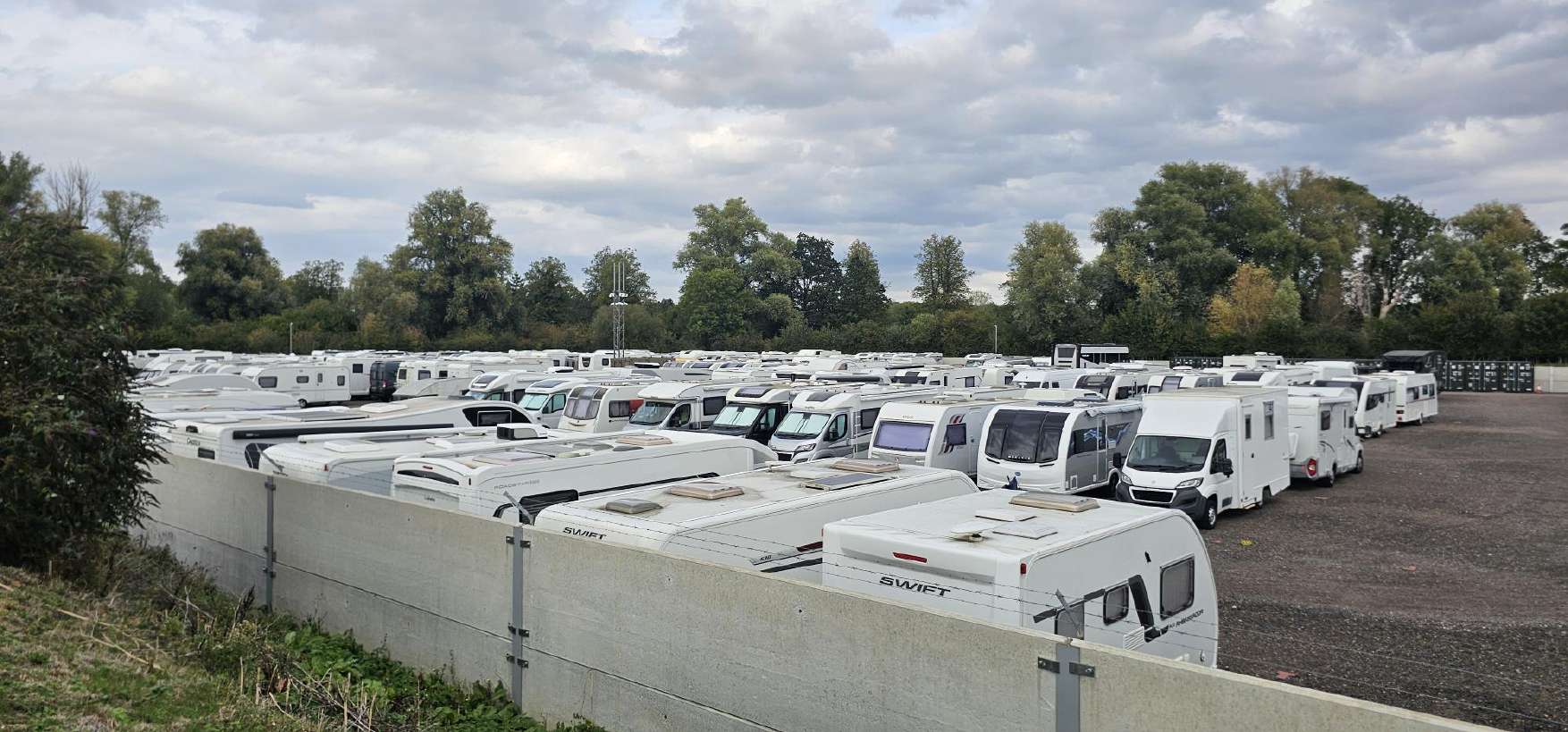 Touring caravans and motorhomes in rows, seen over the concrete perimeter wall