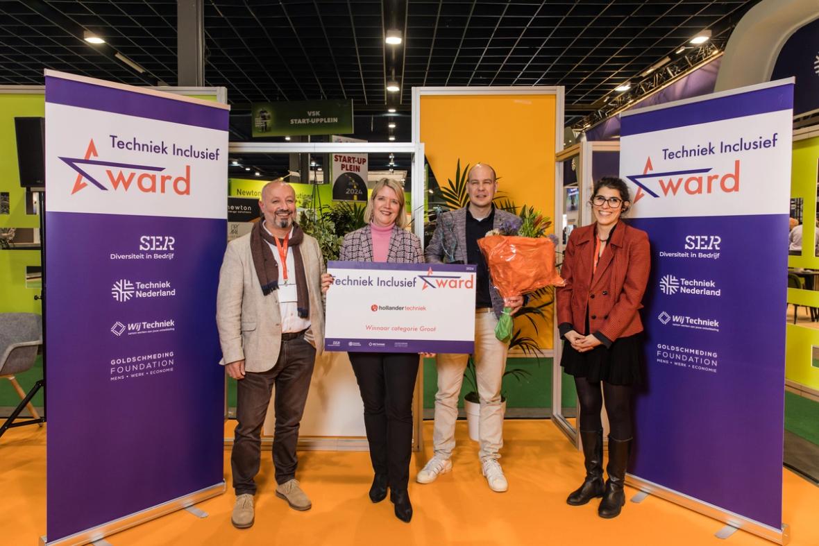 Vier lachende Finalisten van de Techniek Inclusief Award kijken lachend naar de camera met grote voucher voor zich waarop staat Hollander Techniek.
