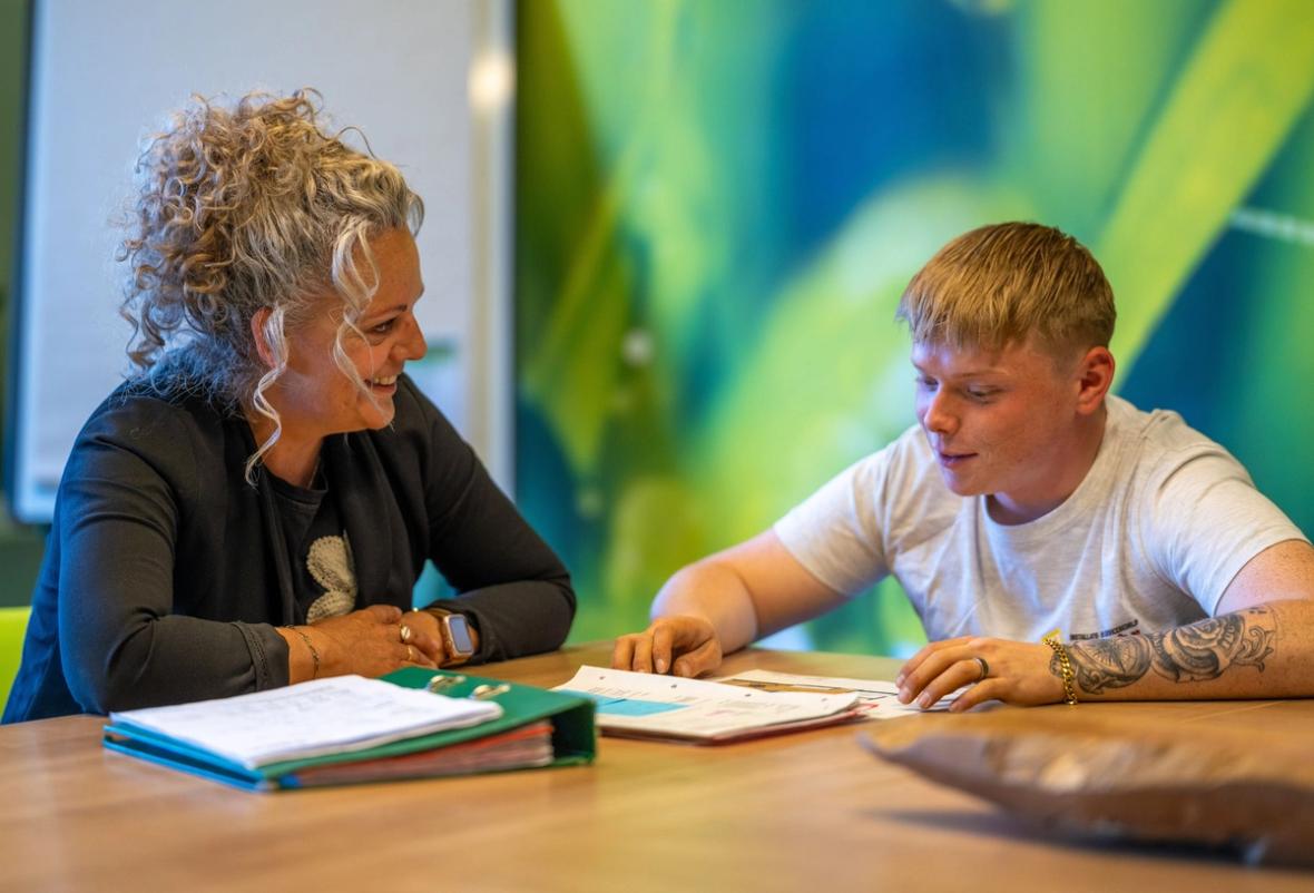 Lachende vrouwelijke praktijkopleider en jonge leerling van Installatiebedrijf De Haan in gesprek aan tafel