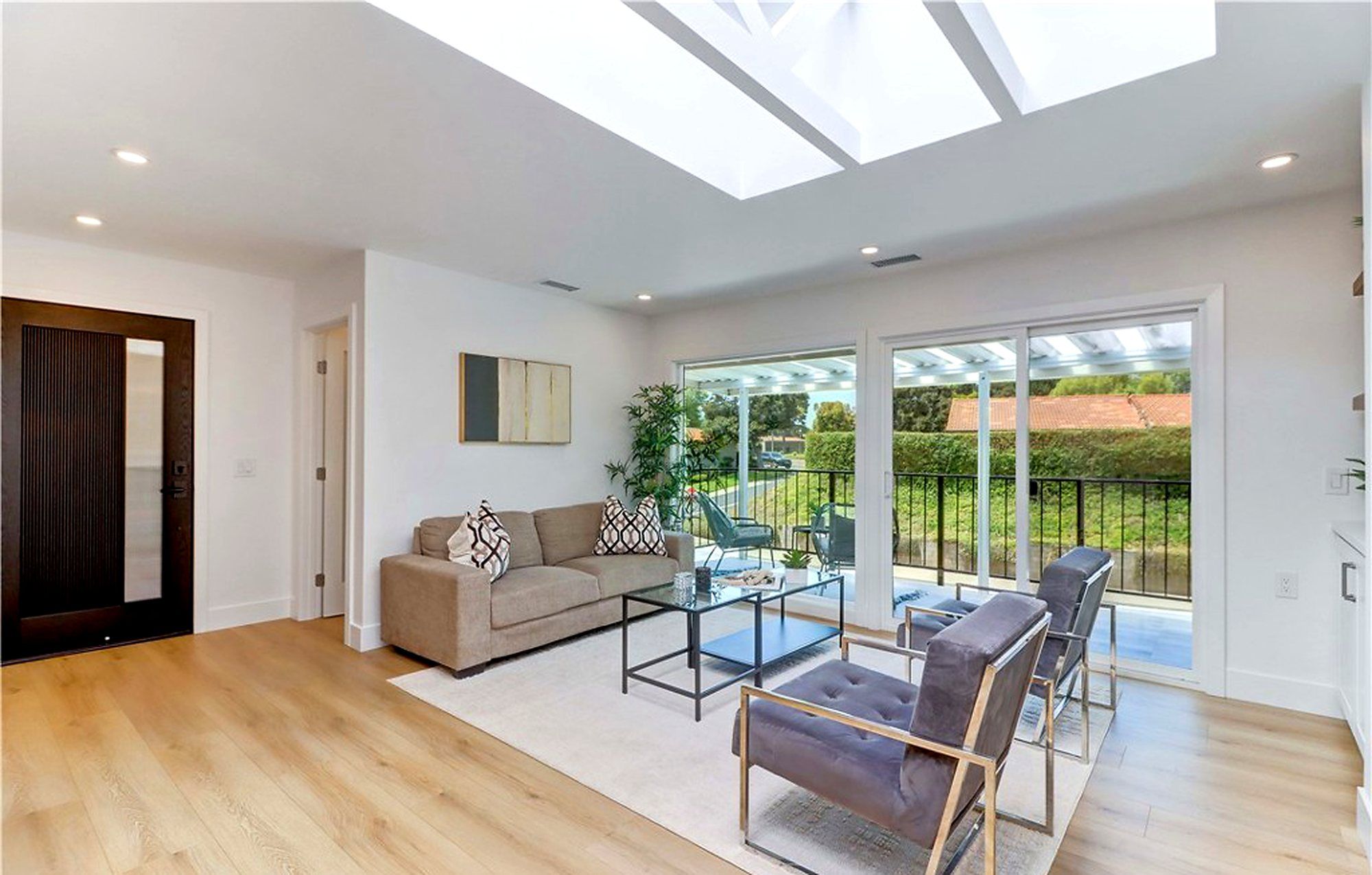 Living room with a tan sofa and gray armchairs under a skylight, open to the balcony, Laguna Woods