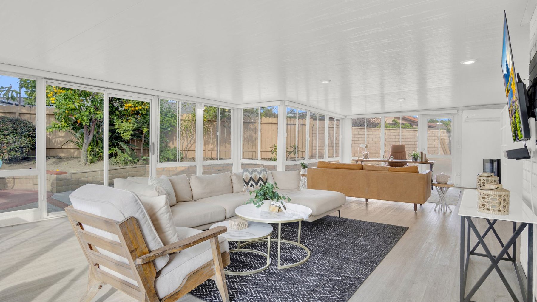 A staged sunroom with white seating and round nesting tables