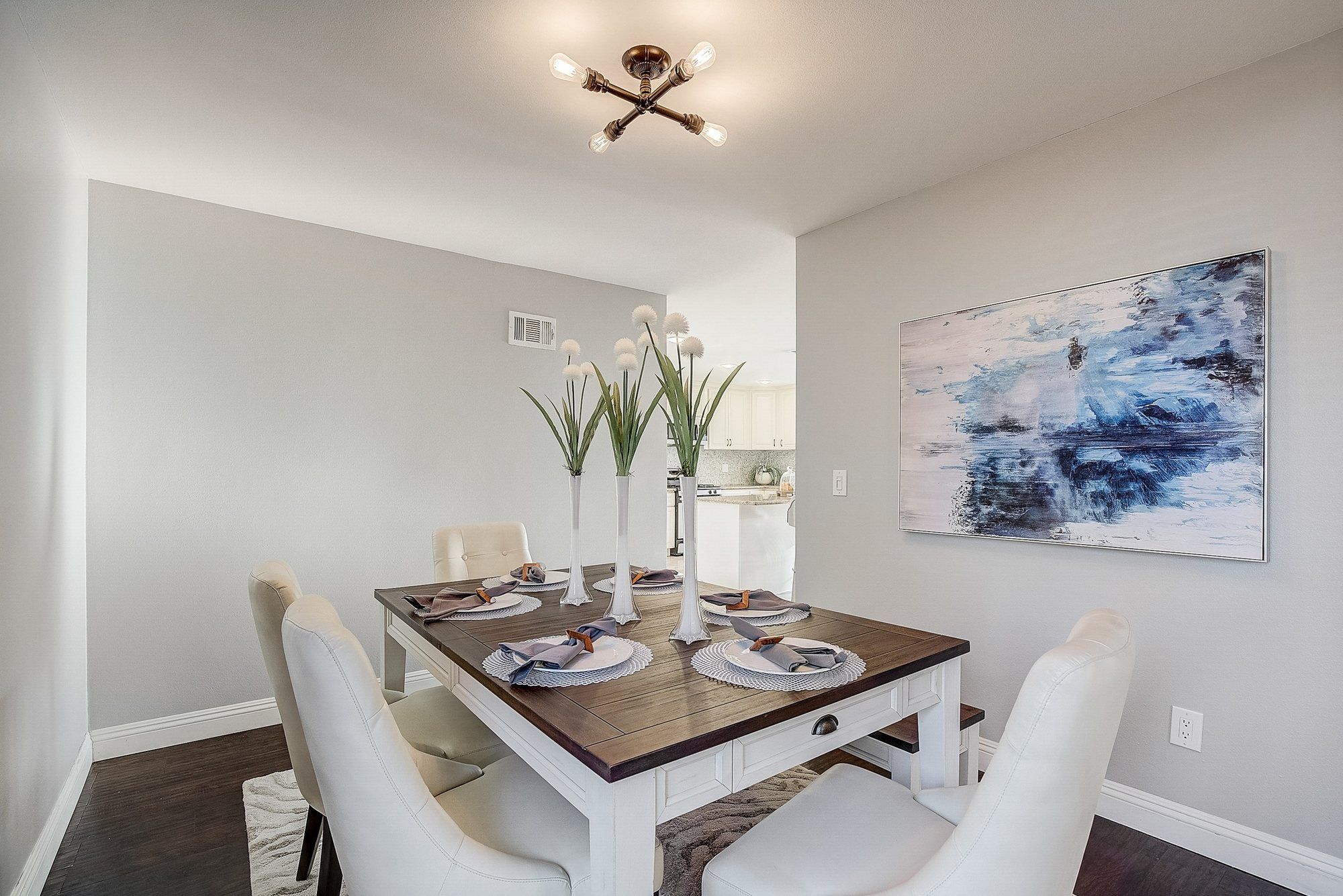 White dining table with a dark top, cream chairs and blue abstract art, Huntington Beach