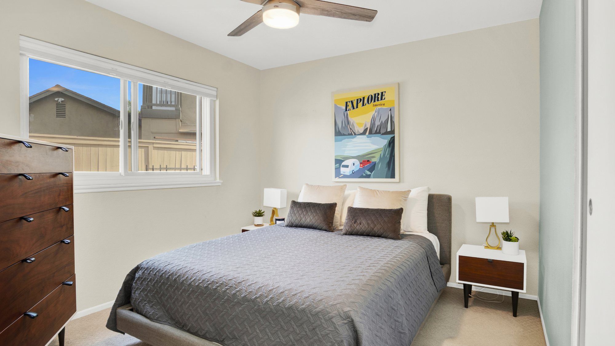 Bedroom with gray bedding, wood nightstands and a travel poster, Dana Point