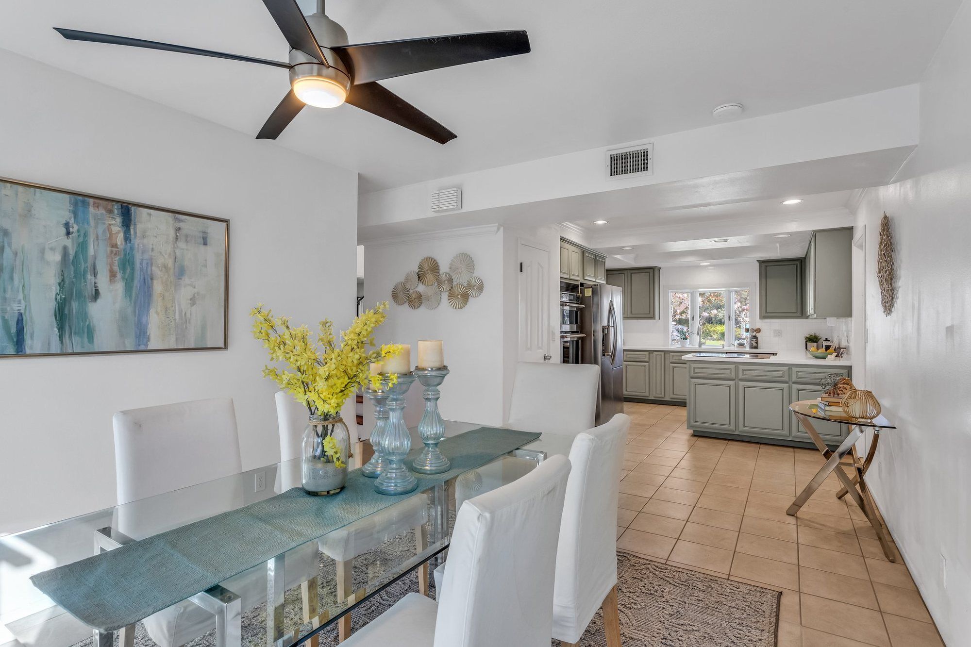 Glass dining table with a teal runner and yellow flowers, open to the kitchen, Tustin
