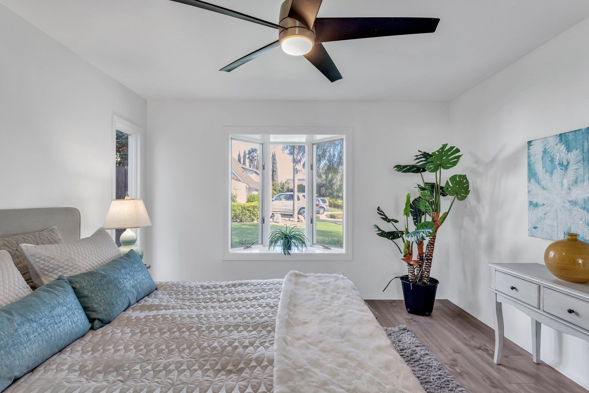 Bed with a patterned coverlet and a tall plant by the window, Tustin