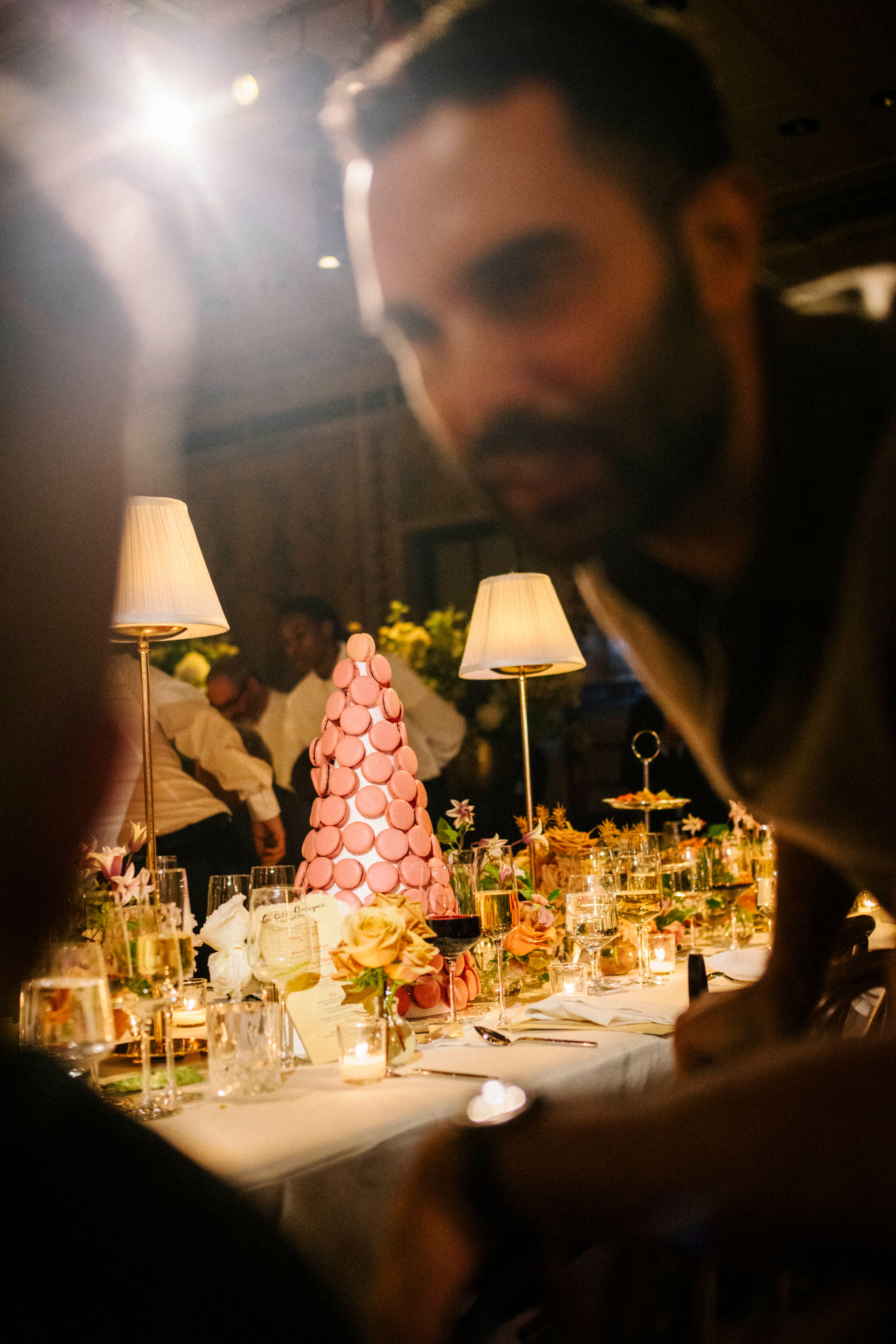 Man speaking to another guest in foreground; macaron tower on dinner table in background