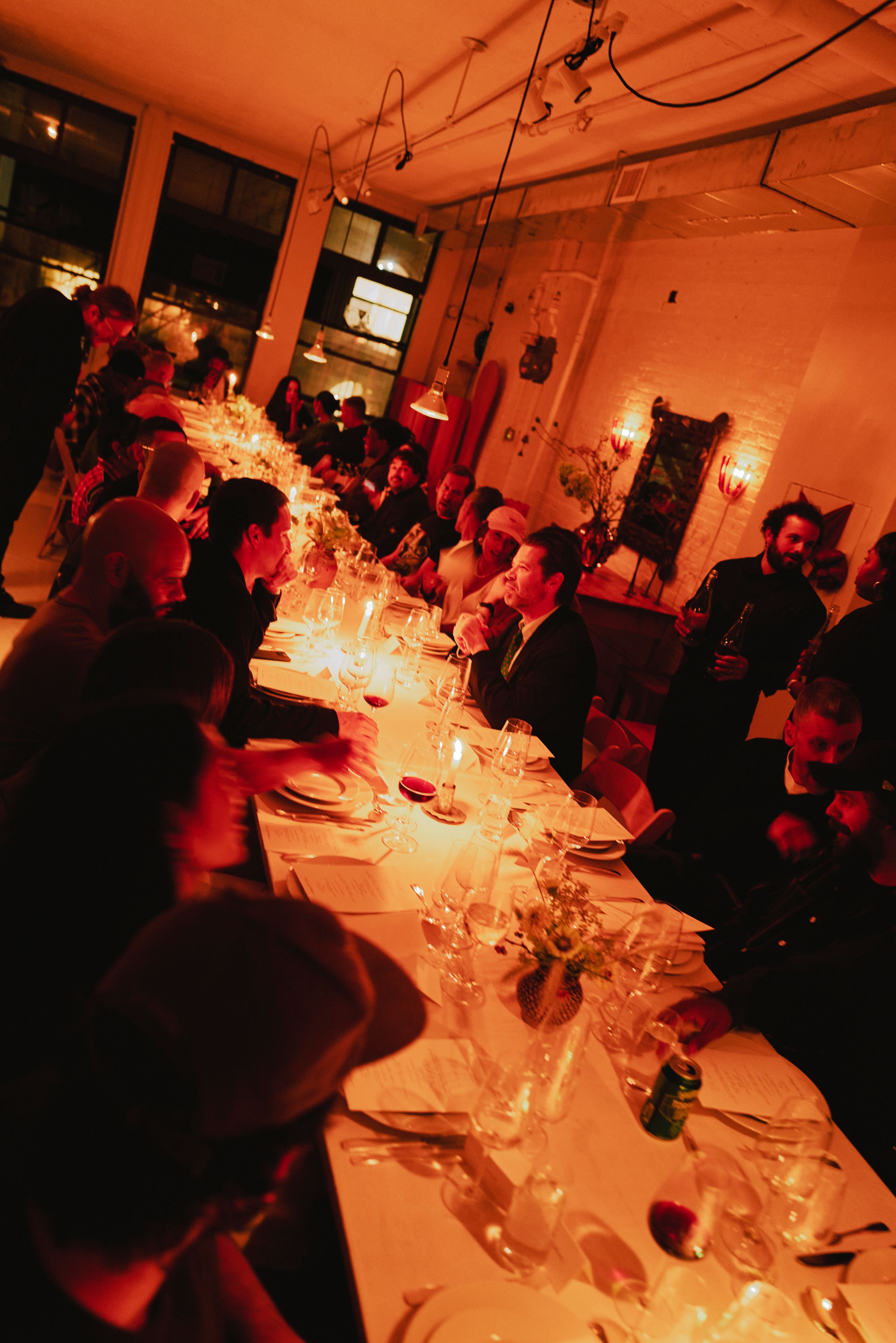 People gathered around long dinner table under moody orange lighting