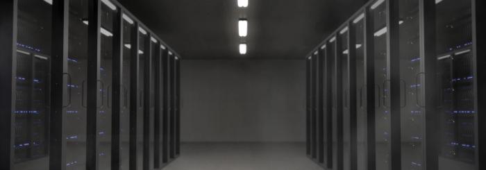 A dark server room with rows of racks and a lit corridor