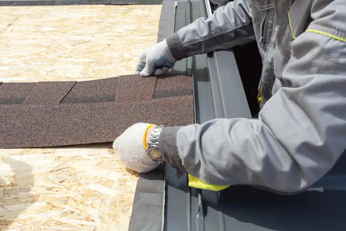 A male contractor laying down asphalt shingle sheets on a home's roof - Roof replacement materials