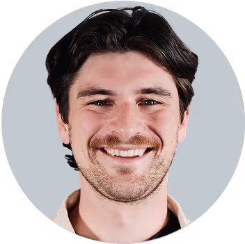 Man with dark hair smiling at camera against light gray background
