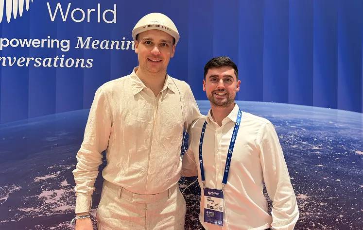 Two men standing together in front of a blue backdrop with Earth imagery, both wearing white shirts
