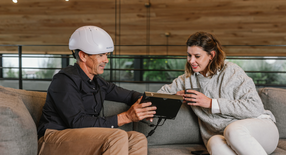 Man wearing white Neuronic Helmet sitting on couch with woman reviewing tablet together