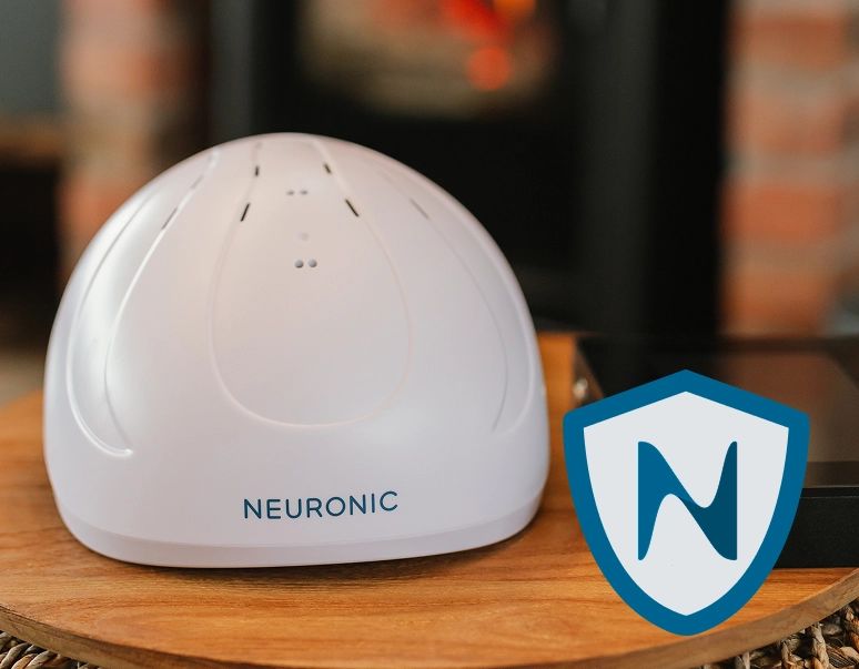 Man wearing white Neuronic headset, holding control tablet while seated on couch