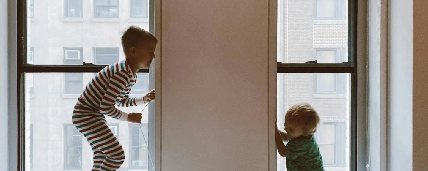 Two young children looking out of a window at apartment buildings