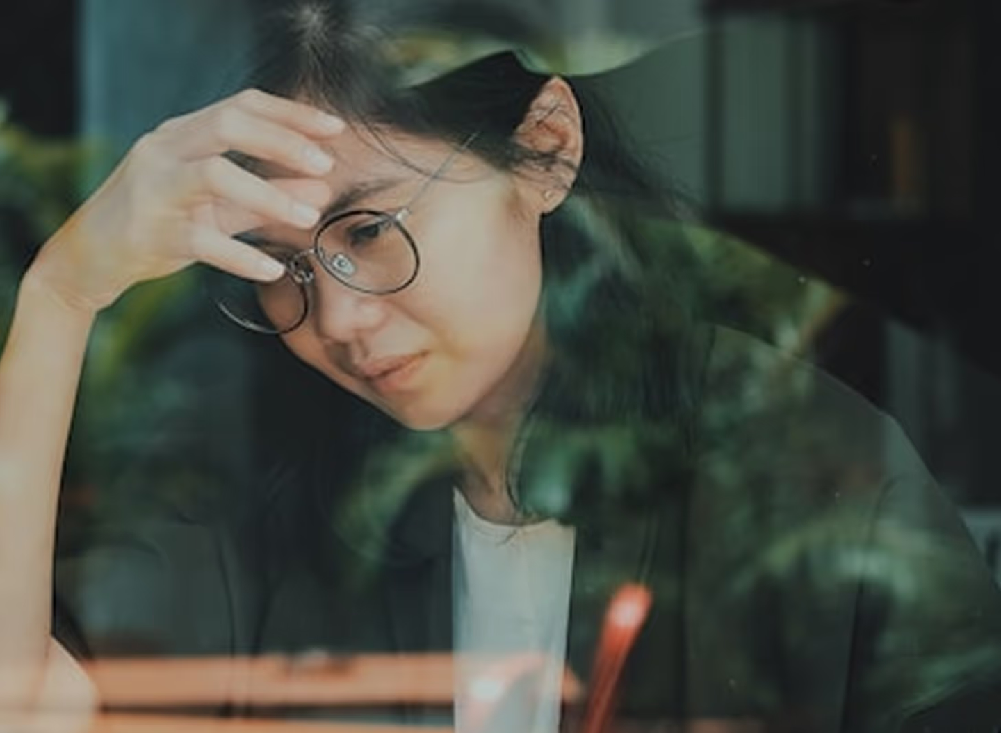 Person wearing glasses with hand raised to head, looking downward
