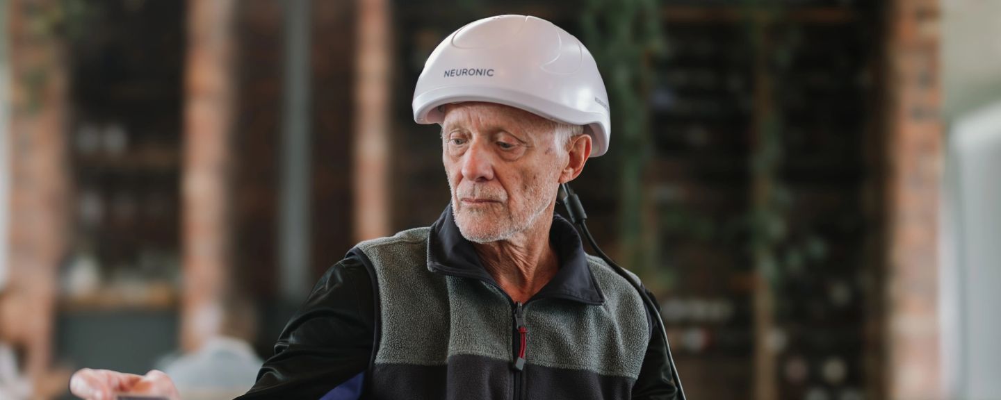 Older man wearing Neuronic Helmet, looking downward outdoors