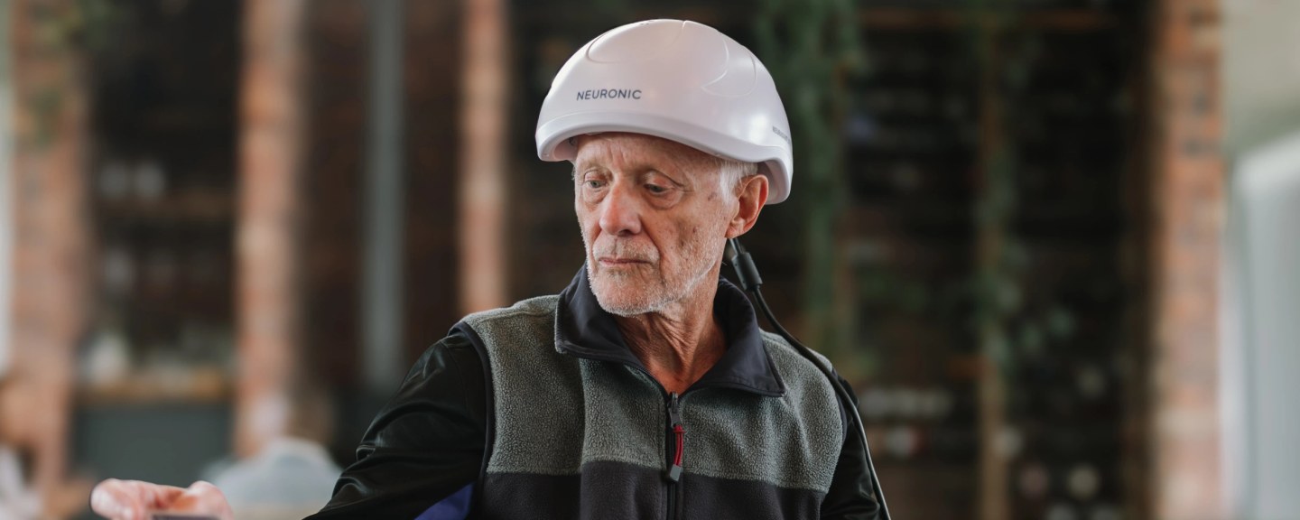 Older man wearing Neuronic Helmet, looking downward outdoors
