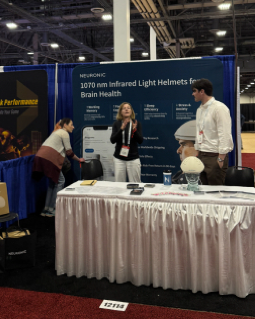 Neuronic booth at conference with staff demonstrating 1070 nm infrared light helmets for brain health to visitors