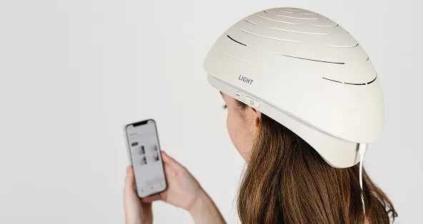 Woman wearing Neuronic LIGHT helmet, holding smartphone displaying control interface