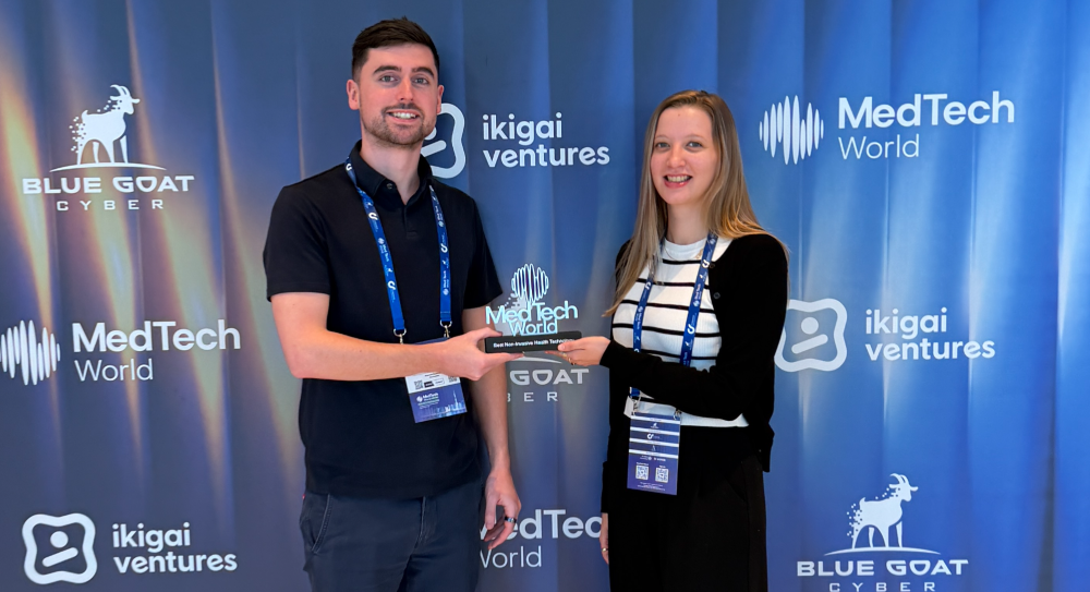 Two people wearing conference badges shake hands while holding an award at a MedTech World event