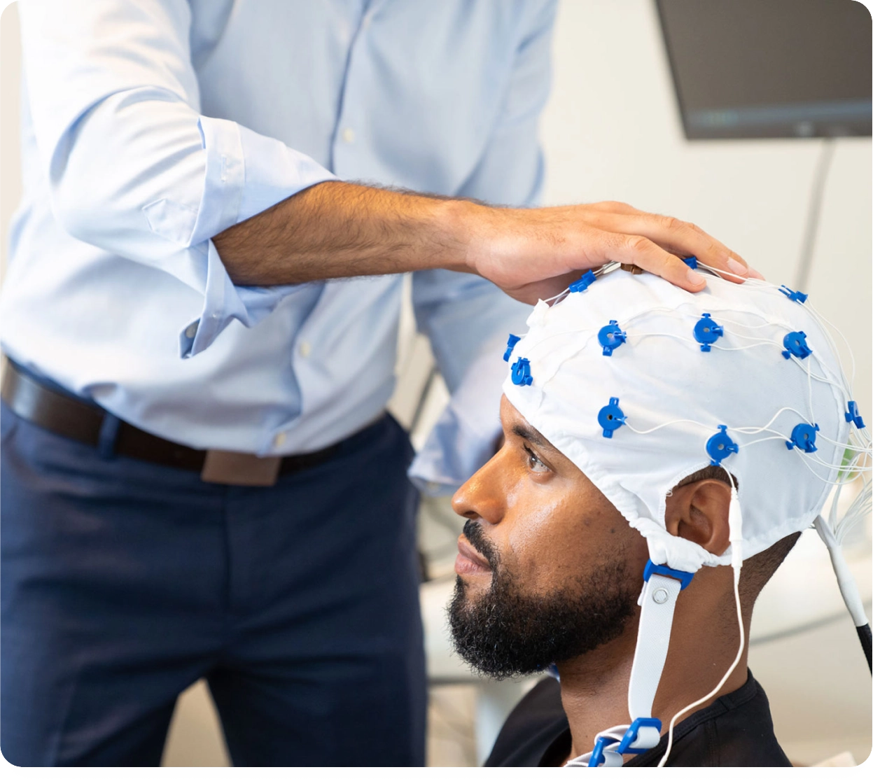 Clinician adjusting an EEG cap with blue electrodes on a patient's head during a brain imaging session