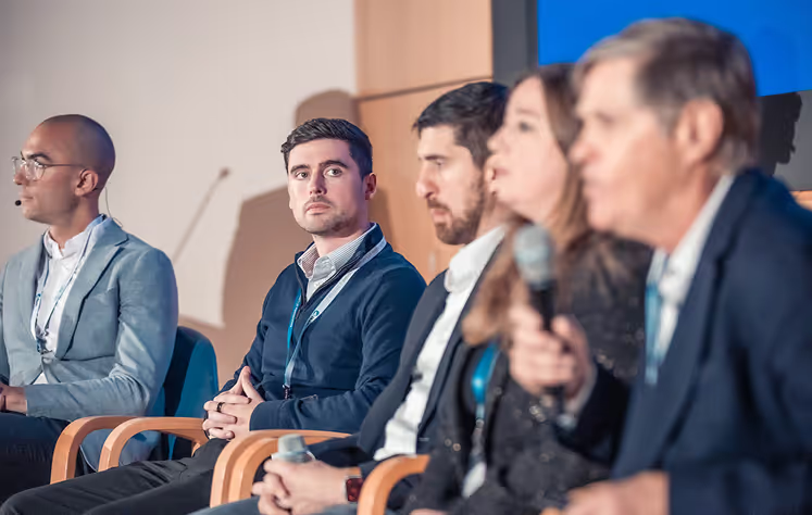 Five professionals seated together at a panel discussion, listening to a speaker