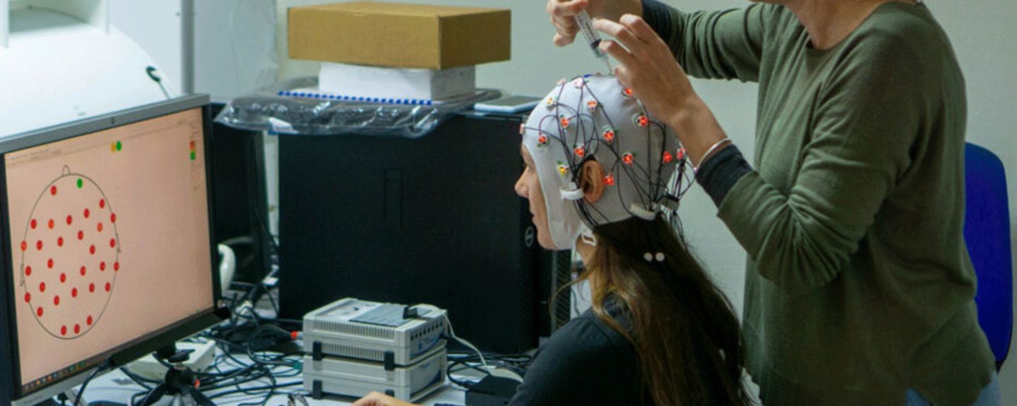 Person wearing EEG electrode cap with red and yellow markers while technician adjusts the fit during neural measurement setup