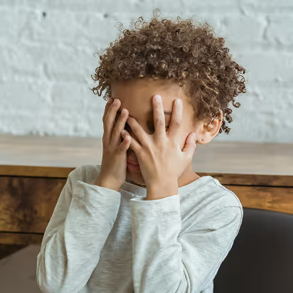 Child with curly hair covering face with both hands
