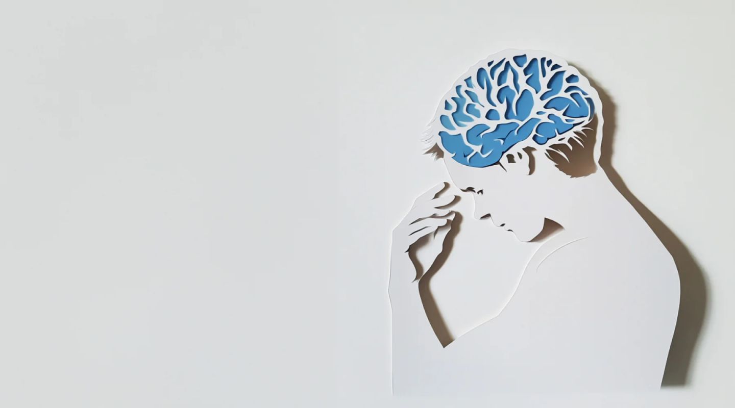 Papercut illustration of a person in profile with a blue brain visible inside the head, hand raised to chin in a thinking pose