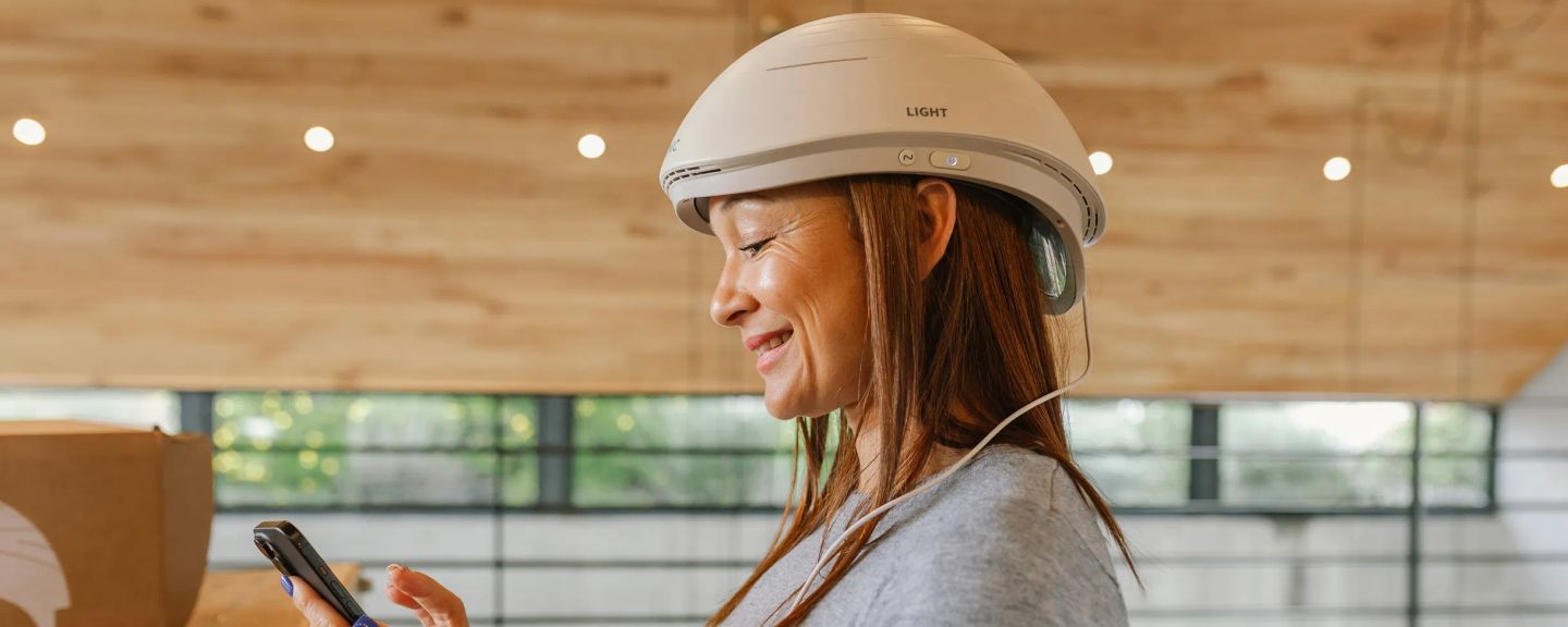 Woman wearing Neuronic Helmet, smiling and holding a smartphone