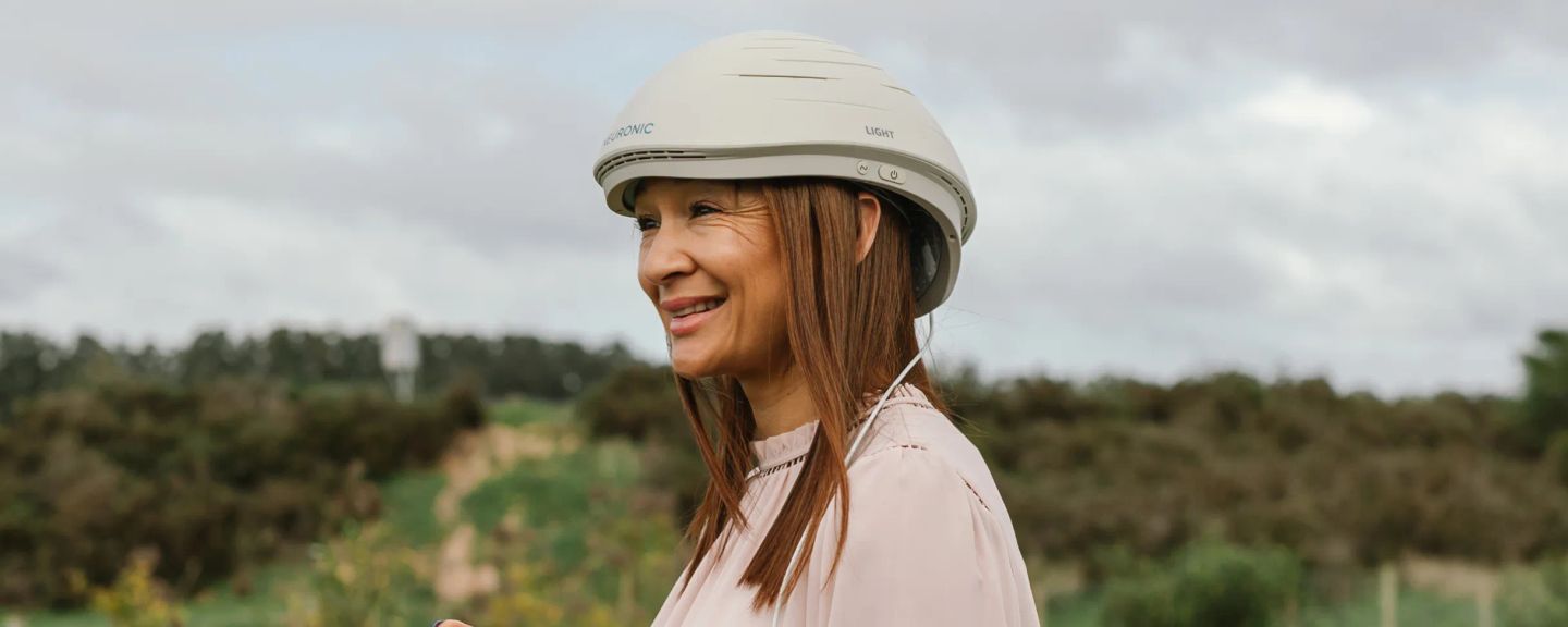 Woman wearing the Neuronic Helmet, smiling outdoors with agricultural field in background